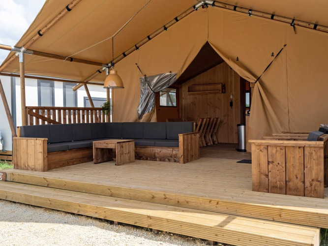 Spacious glamping tent with wooden deck, large sofa, and cozy seating area in a campsite setting.