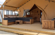 Tienda de glamping con terraza de madera, sofá amplio y área de descanso en un alojamiento de lujo.
