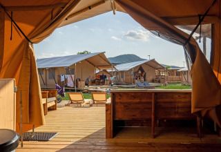 Udsigt fra et luksustelt over en glampingplads med moderne telte, liggestole og bjerge i baggrunden.