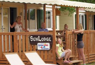 Familia disfruta en el porche de madera del SunLodge Maple en hu Norcenni Girasole Village, Italia.