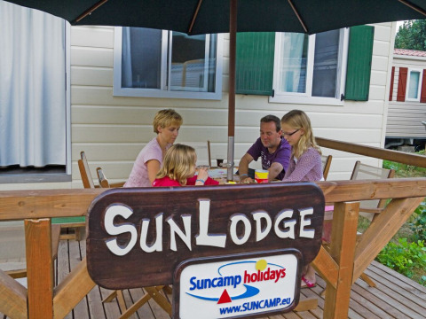 Een familie geniet aan tafel onder een parasol bij SunLodge Maple, hu Norcenni Girasole Village in Italië.
