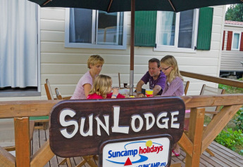 Een familie geniet aan tafel onder een parasol bij SunLodge Maple, hu Norcenni Girasole Village in Italië.