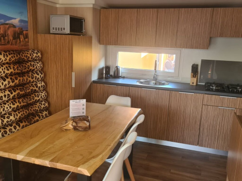 Moderne køkken i SunLodge Babul med trædetaljer, spisebord, leopardmønstrede hynder og vindue.