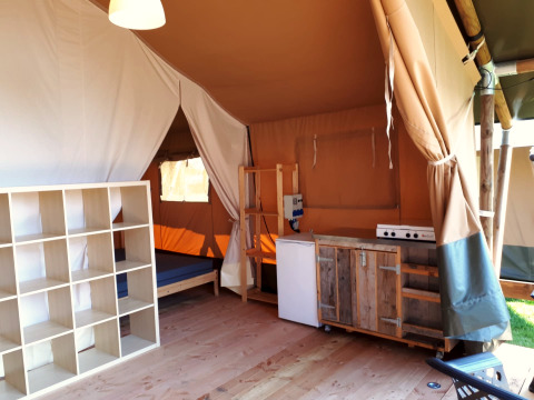 Interieur van een safaritent met keuken, schappen en bed bij Camping Oos Heem in België.