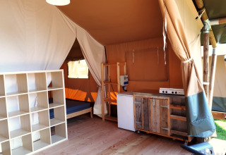 Interieur van een safaritent met keuken, schappen en bed bij Camping Oos Heem in België.