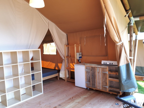 Interior de una tienda safari con cocina, estantería y cama en Camping Oos Heem, Bélgica.