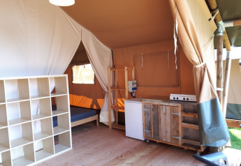 Interior of a safari tent with a kitchen, shelving, and bed at Camping Oos Heem in Belgium.