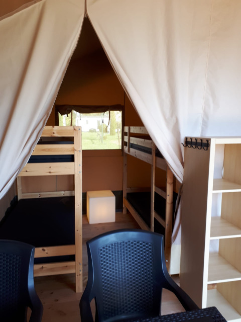 Indretning af en safaritelt på Camping Oos Heem i Belgien med køjesenge, stole og reol.