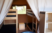 Interno di una tenda safari al Camping Oos Heem in Belgio con letti a castello, sedie e scaffali.