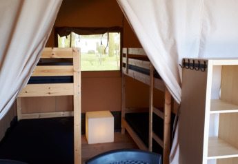 Interior de una tienda safari en Camping Oos Heem en Bélgica con literas, sillas y estanterías.