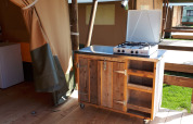Cocina exterior con estufa de gas en una tienda safari en Camping Oos Heem, Bélgica, mueble de madera.