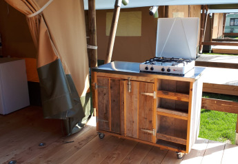 Cocina exterior con estufa de gas en una tienda safari en Camping Oos Heem, Bélgica, mueble de madera.