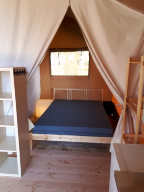 Interieur van een safaritent op Camping Oos Heem in België met bed, planken en houten vloer.