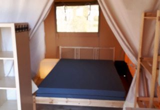 Interieur van een safaritent op Camping Oos Heem in België met bed, planken en houten vloer.