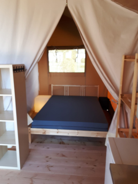 Interior de una tienda safari en Camping Oos Heem, Bélgica, con cama, estanterías y suelo de madera.