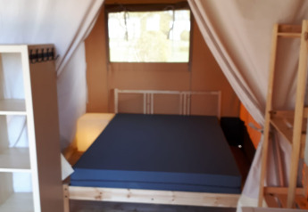 Interior de una tienda safari en Camping Oos Heem, Bélgica, con cama, estanterías y suelo de madera.