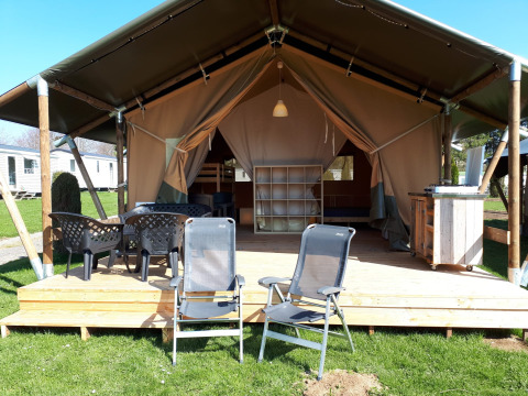 Tienda safari en Camping Oos Heem en Bélgica, con terraza de madera, sillas y ambiente acogedor.