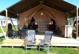 Tienda safari en Camping Oos Heem en Bélgica, con terraza de madera, sillas y ambiente acogedor.
