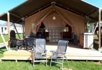 Tienda safari en Camping Oos Heem en Bélgica, con terraza de madera, sillas y ambiente acogedor.