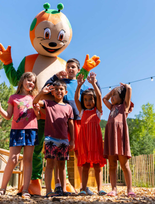 Children with a colorful mascot posing outdoors at Camping La Presqu’île holiday park in southern France.