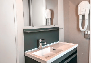 Moderno lavabo de baño con espejo y secador de pelo en Forest Lodge del Vakantiepark De Luttenberg, Países Bajos.