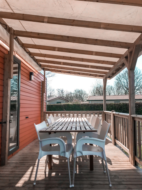 Terraza cubierta con mesa de madera y sillas blancas en Forest Lodge, Vakantiepark De Luttenberg, Países Bajos.