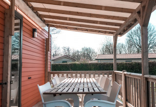 Terraza cubierta con mesa de madera y sillas blancas en Forest Lodge, Vakantiepark De Luttenberg, Países Bajos.