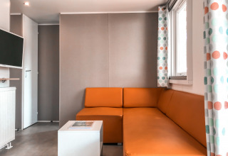 Salón moderno en Forest lodge del Vakantiepark De Luttenberg, con sofá naranja y cortinas de colores.