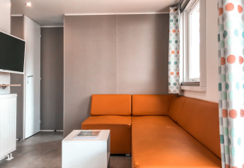 Moderne stue i Forest lodge ved Vakantiepark De Luttenberg, med orange sofa og farverige gardiner.