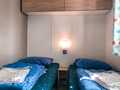 Dos camas individuales con sábanas azules en una habitación Forest Lodge en Vakantiepark De Luttenberg, Países Bajos.