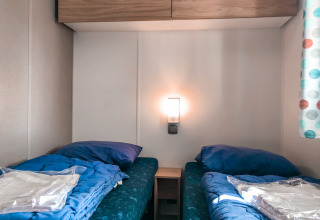 Dos camas individuales con sábanas azules en una habitación Forest Lodge en Vakantiepark De Luttenberg, Países Bajos.