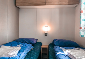 To enkeltsenge med blåt sengetøj på et Forest Lodge-værelse i Vakantiepark De Luttenberg, Holland.