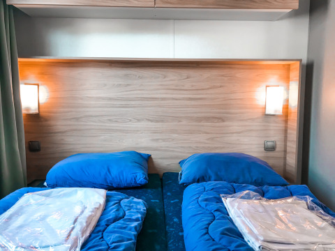 Camas gemelas con ropa de cama azul en Forest lodge de Vakantiepark De Luttenberg en los Países Bajos.