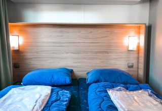 Camas gemelas con ropa de cama azul en Forest lodge de Vakantiepark De Luttenberg en los Países Bajos.