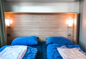 To enkeltsenge med blå sengetøj og træpanelvæg på Forest lodge i Vakantiepark De Luttenberg, Holland.