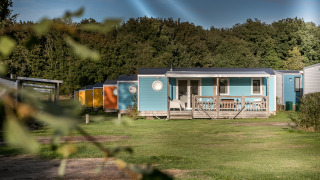 Cabañas móviles coloridas con porches frente a césped y bosque, foto tomada en Forest Lodge.