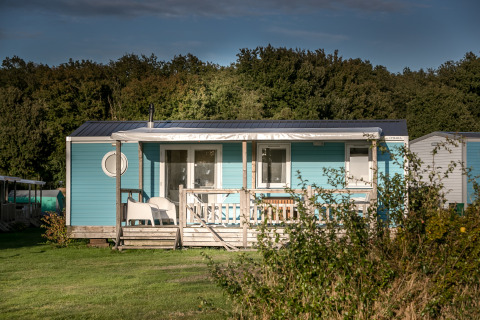 Blauwe Forest lodge bij Vakantiepark De Luttenberg in Nederland, omgeven door gras en bomen.