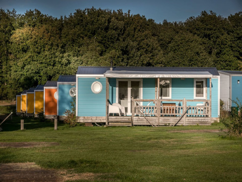 Cabañas coloridas con porche en Forest lodge, Vakantiepark De Luttenberg, Países Bajos, rodeadas de bosque.