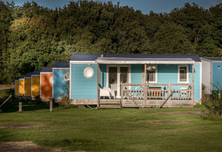 Cabañas coloridas con porche en Forest lodge, Vakantiepark De Luttenberg, Países Bajos, rodeadas de bosque.