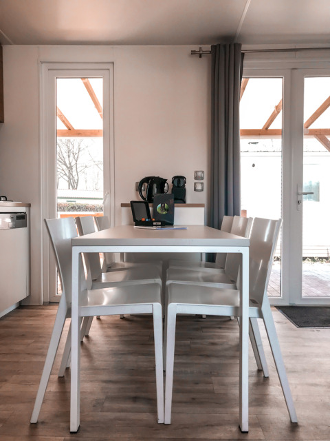 Comedor moderno en Forest Lodge de Vakantiepark De Luttenberg con mesa blanca, sillas y luz natural.