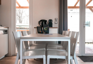 Comedor moderno en Forest Lodge de Vakantiepark De Luttenberg con mesa blanca, sillas y luz natural.