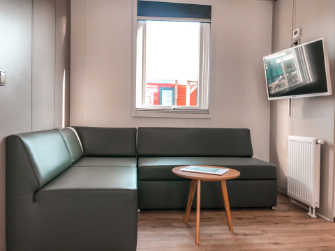 Moderne woonkamer met grijze hoekzetel, flatscreentelevisie, ronde tafel en raam in Forest lodge.