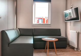 Moderne woonkamer met grijze hoekzetel, flatscreentelevisie, ronde tafel en raam in Forest lodge.