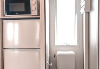 Baño pequeño con inodoro, refrigerador y microondas en Forest lodge, Vakantiepark De Luttenberg, Países Bajos.