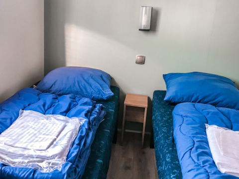Dos camas individuales con ropa de cama azul en Forest Lodge, Vakantiepark De Luttenberg, Países Bajos.