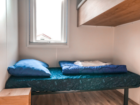 Cama sencilla con ropa azul en Forest lodge de Vakantiepark De Luttenberg, Países Bajos, junto a la ventana.