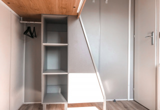 Moderne kast met open rekken en hangers in het Forest Lodge van Vakantiepark De Luttenberg, Nederland.