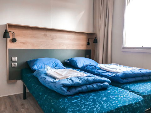 Habitación con dos camas individuales y ropa de cama azul en Forest lodge, Vakantiepark De Luttenberg, Países Bajos.