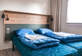 Habitación con dos camas individuales y ropa de cama azul en Forest lodge, Vakantiepark De Luttenberg, Países Bajos.