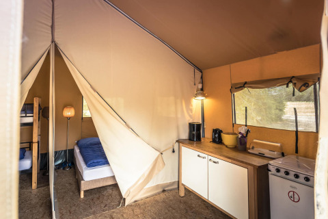 Vista interior de una tienda safari en Vakantiepark De Luttenberg con dormitorio y zona de cocina.